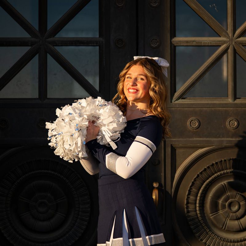 Cheerleader with white pom-poms in front of ornate bronze doors