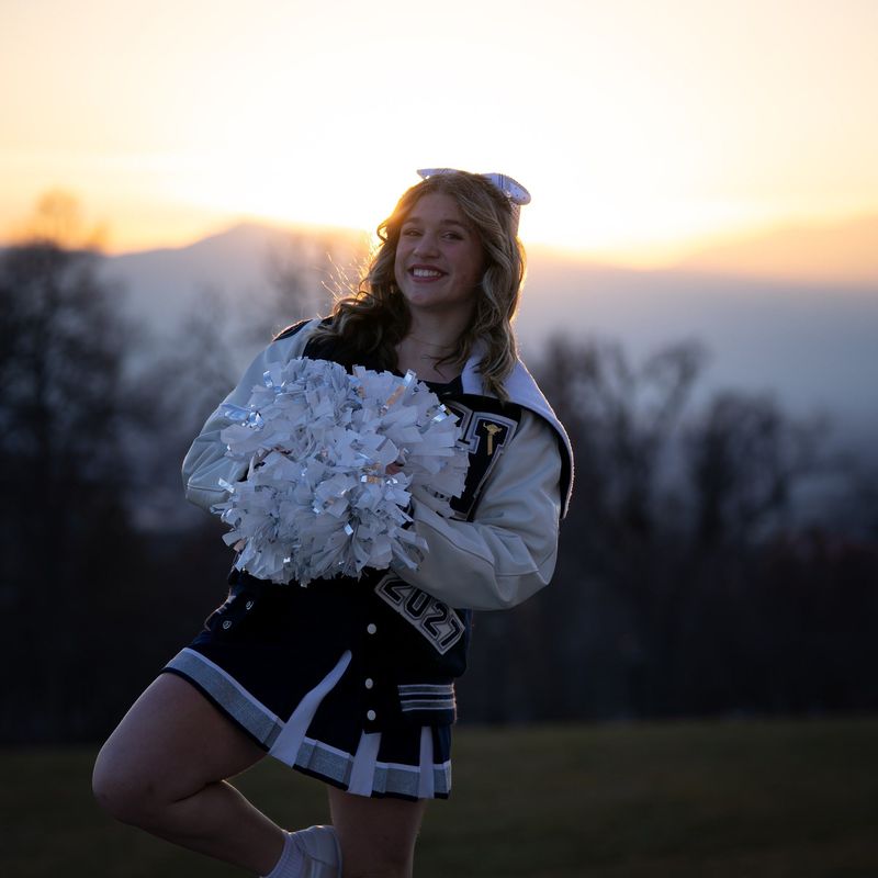 Backlit cheerleader with white pom-poms at sunset, soft mountain horizon