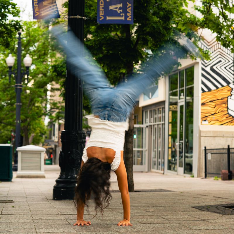 Senior doing a handstand on a downtown sidewalk beside a lamppost