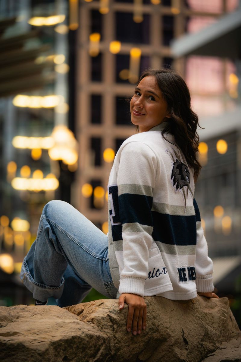 Senior seated on a rock looking over her shoulder, city lights behind