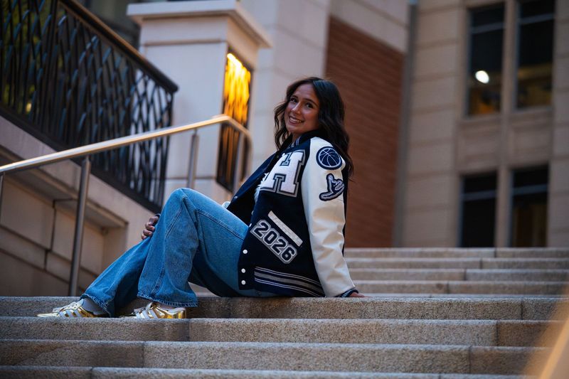 Senior seated on downtown stairs in a letterman jacket, wide frame