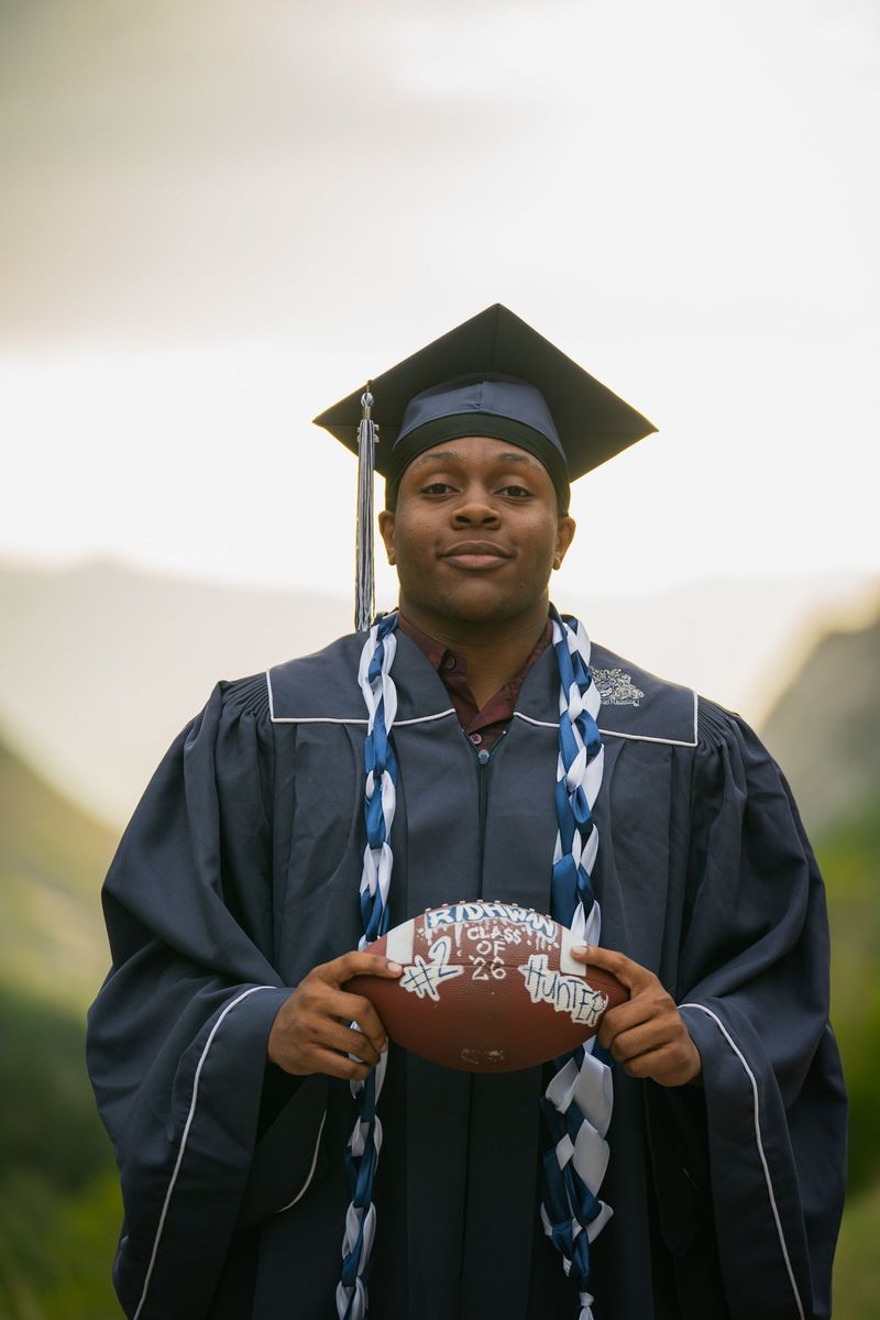 Graduate in cap and gown holding a football, tight frame