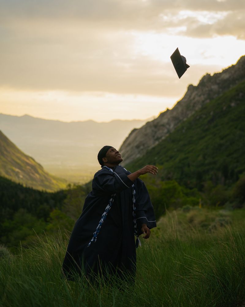 Graduate tossing his cap into the sky above a green mountain valley