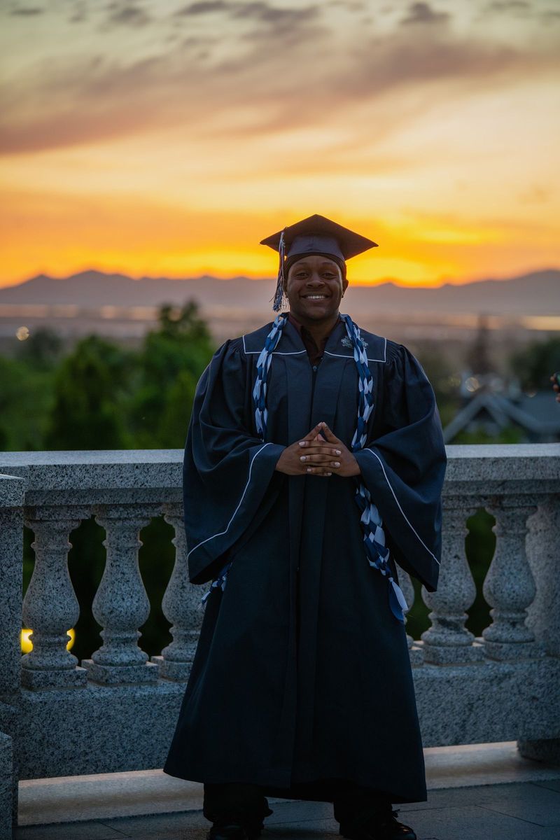 Graduate with hands together on a stone balcony under an orange sunset