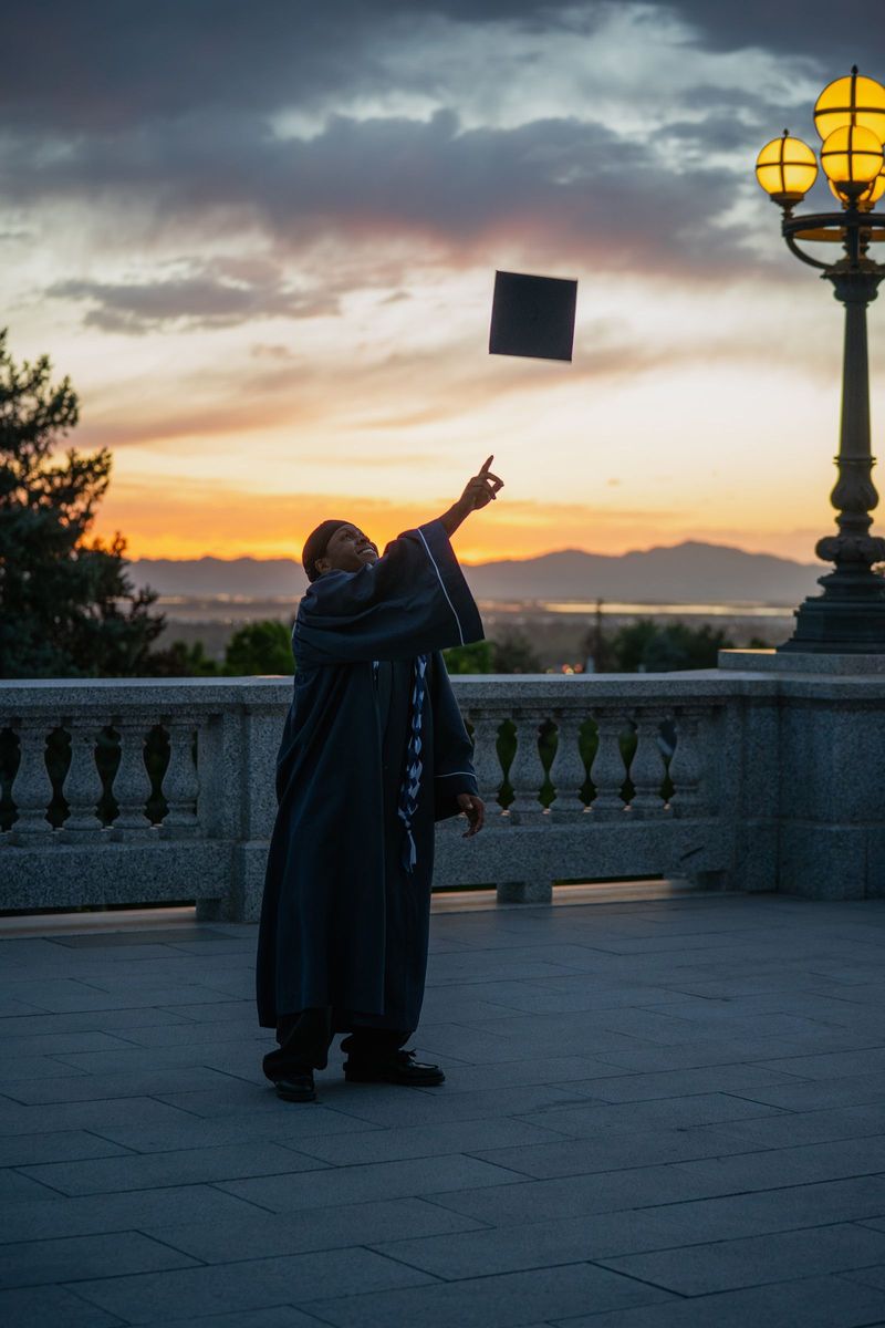 Graduate looking up at a cap tossed against a dusk sky beside a lamppost